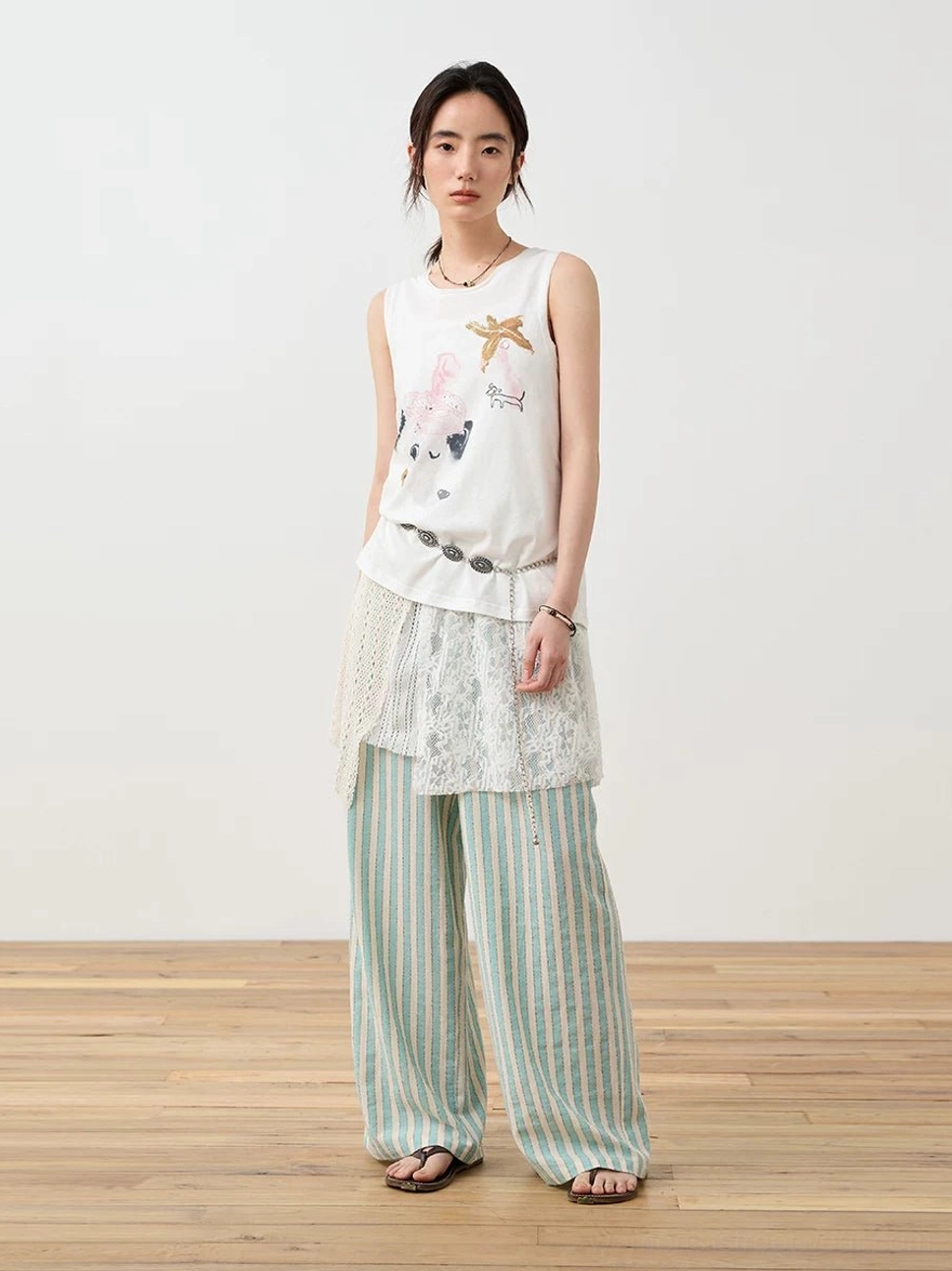 Off-white asymmetric crochet lace cami top layered over a graphic tank with mint green striped wide-leg pants in a Korean streetwear outfit