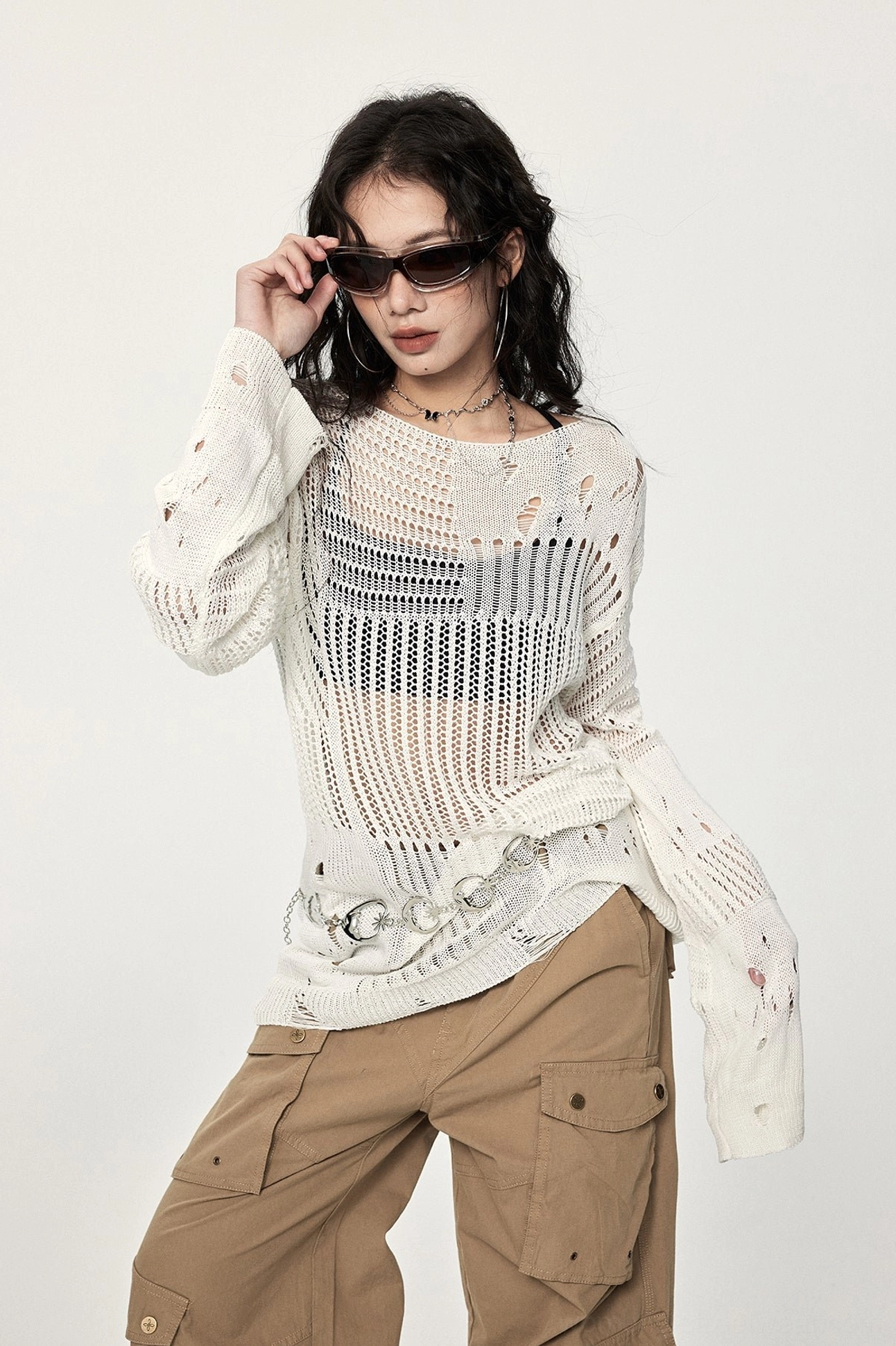 Front styling view of an off-white distressed crochet long-sleeve sweater with loose silhouette, uneven hem, and metal ring streetwear details