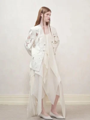 Women’s off-white distressed cutout blazer layered over a flowing asymmetric slip dress three-quarter side view