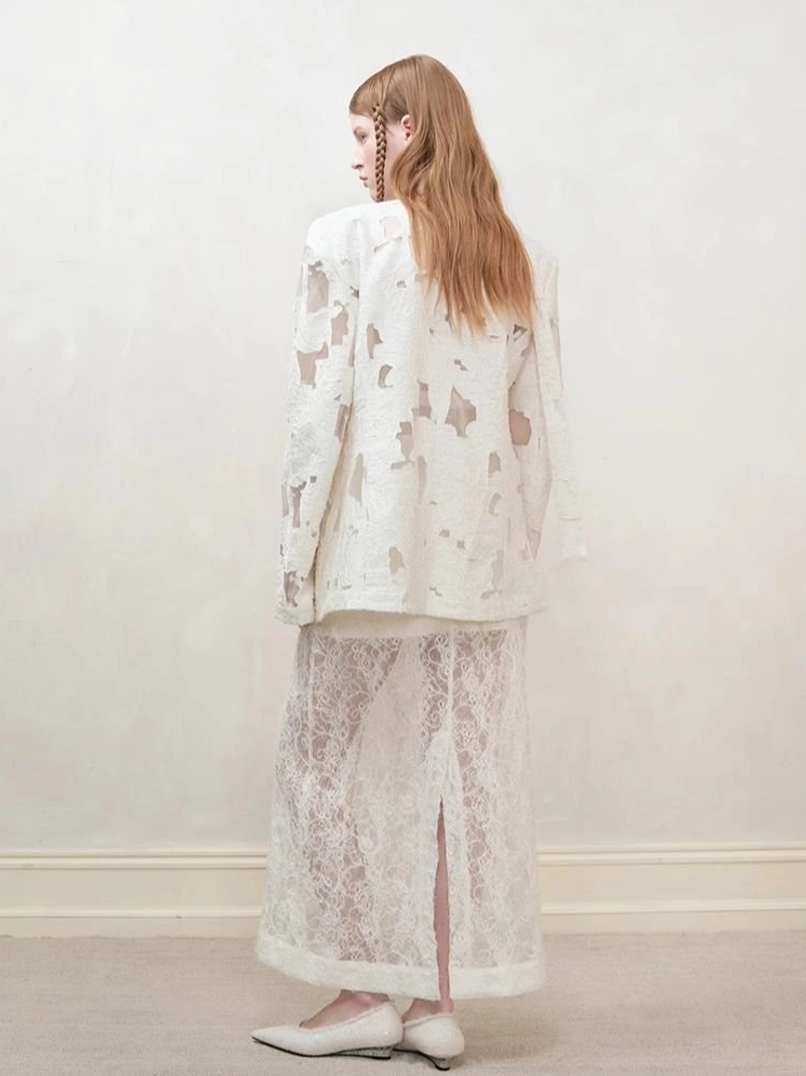 Three-quarter back view of women’s distressed off-white cutout blazer with high-slit lace midi skirt