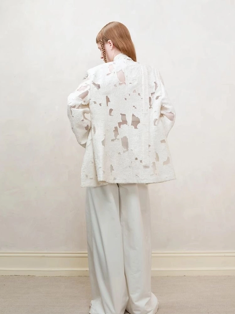Rear view of off-white distressed cutout blazer for women paired with relaxed straight-leg white trousers