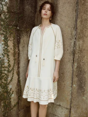 Off-white embroidered shift dress with tassel tie neckline, three-quarter puff sleeves, and geometric hem embroidery