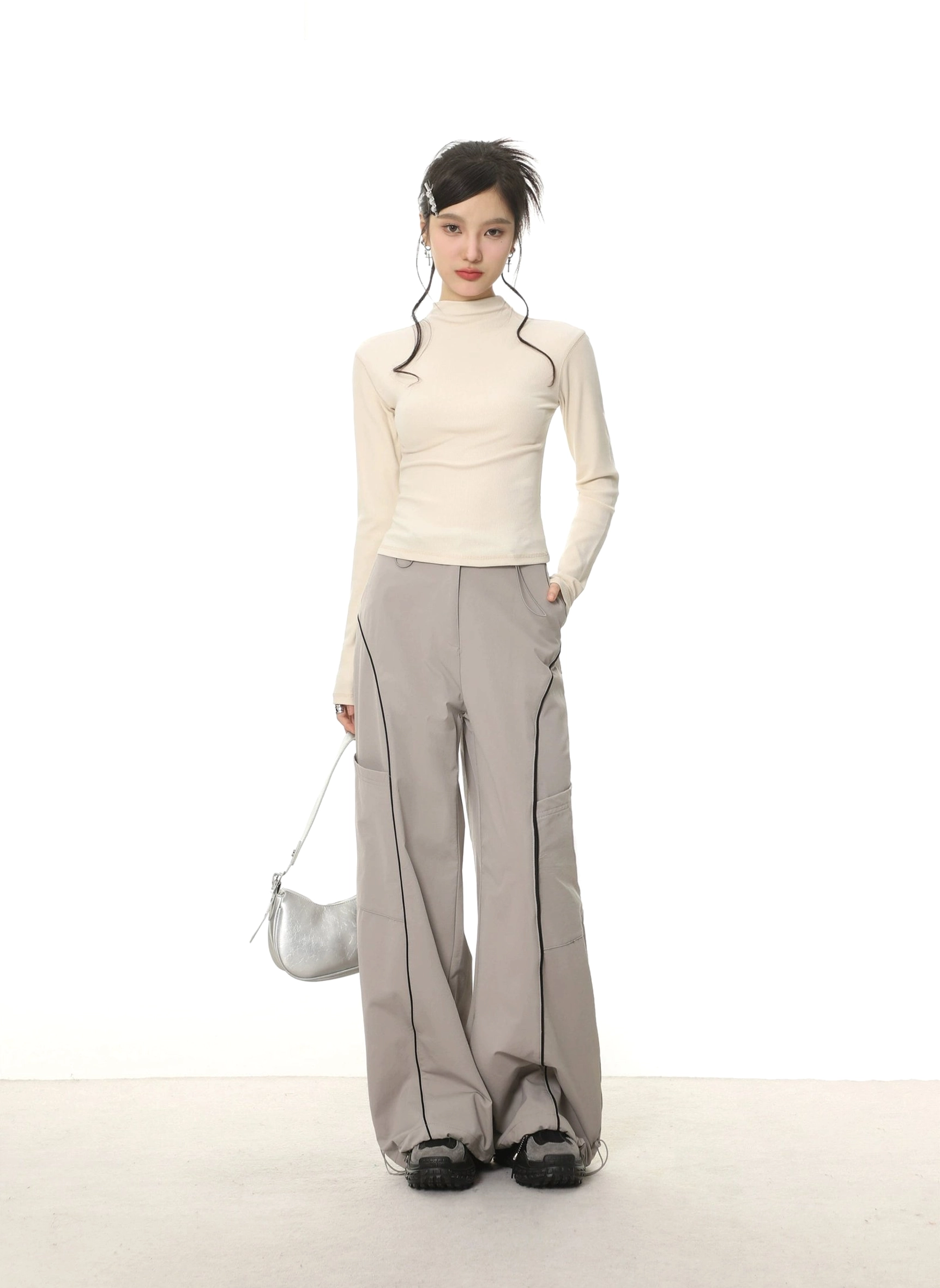Off-white fitted mock neck long sleeve streetwear top paired with grey wide-leg cargo pants and metallic handbag