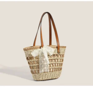 Off white woven straw basket tote bag with detachable white lace bow, brown shoulder straps, and structured summer streetwear silhouette