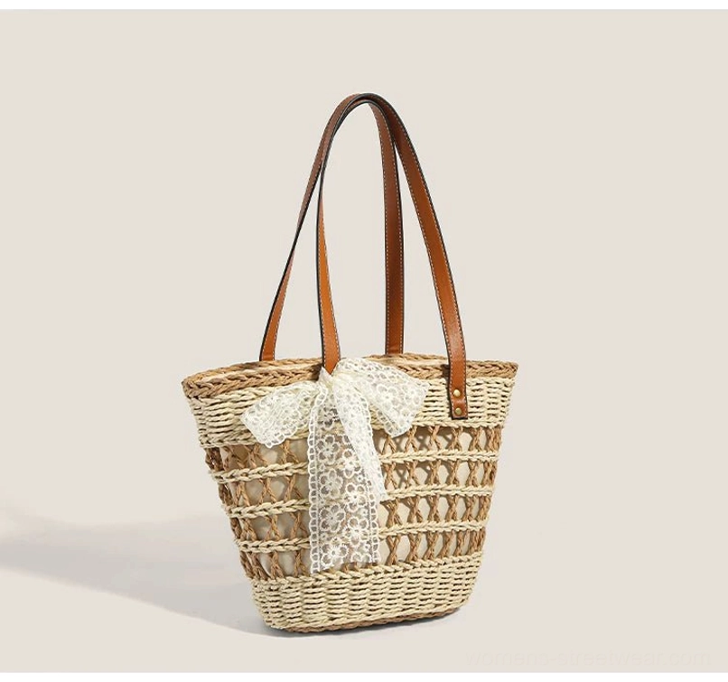 Off white woven straw basket tote bag with detachable white lace bow, brown shoulder straps, and structured summer streetwear silhouette