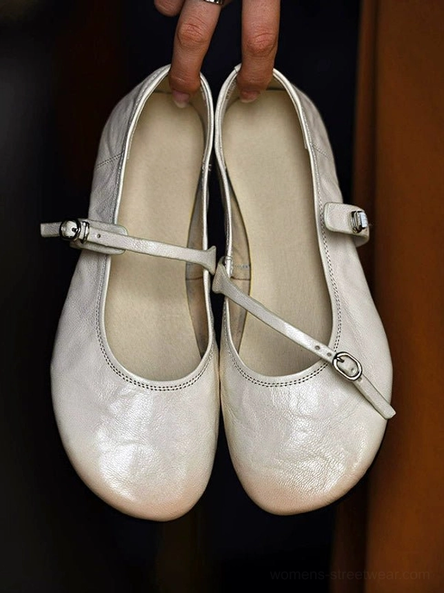 Overhead view of ivory Mary Jane flat shoes held by the openings, showing the padded pigskin insole, rounded toe shape, and matching buckle straps