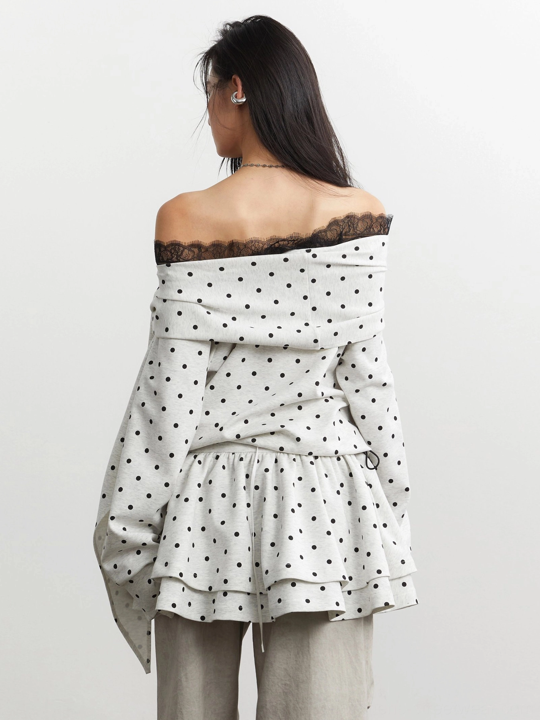 Back view of an off-white polka dot off-shoulder peplum top with black lace trim, double-layer ruffled hem, and draped sleeve detail