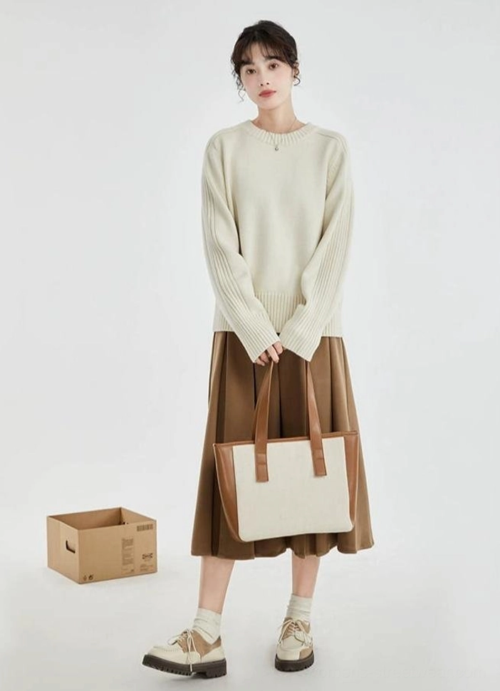 Full body styling of an off-white ribbed crewneck sweater with brown pleated skirt, loafers, ankle socks, and two-tone tote bag