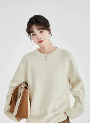 Full front view of an off-white ribbed knit crewneck sweater with relaxed drop shoulders styled with a brown pleated skirt and leather tote