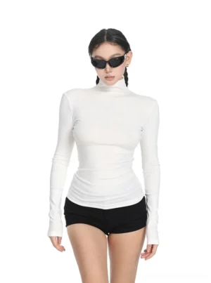 Off-white fitted turtleneck top for women with long sleeves and slim stretch knit silhouette styled with black mini shorts and cat-eye sunglasses