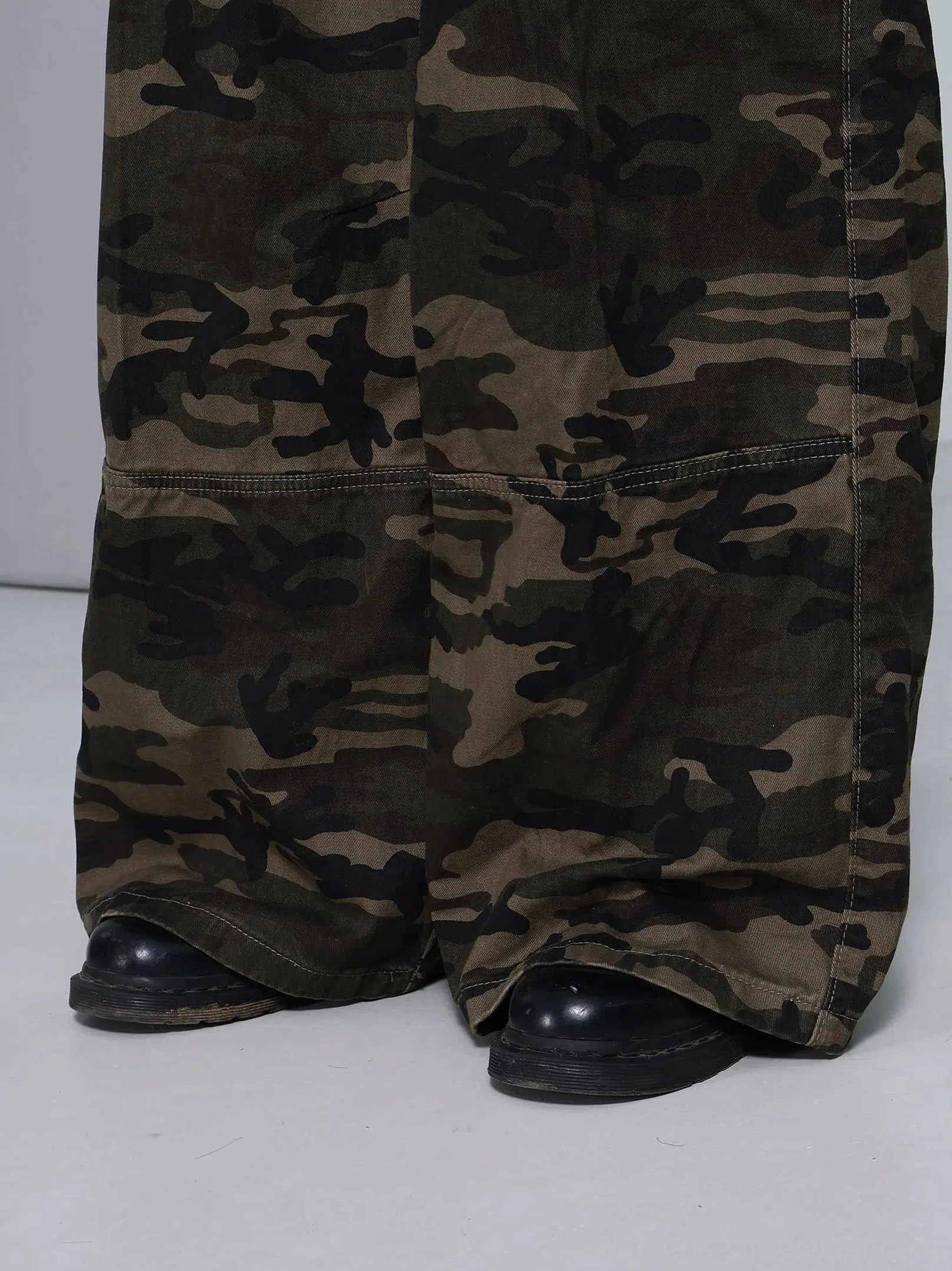 Close-up of reinforced wide leg hems and structured panels on olive woodland camouflage cargo pants styled with black shoes