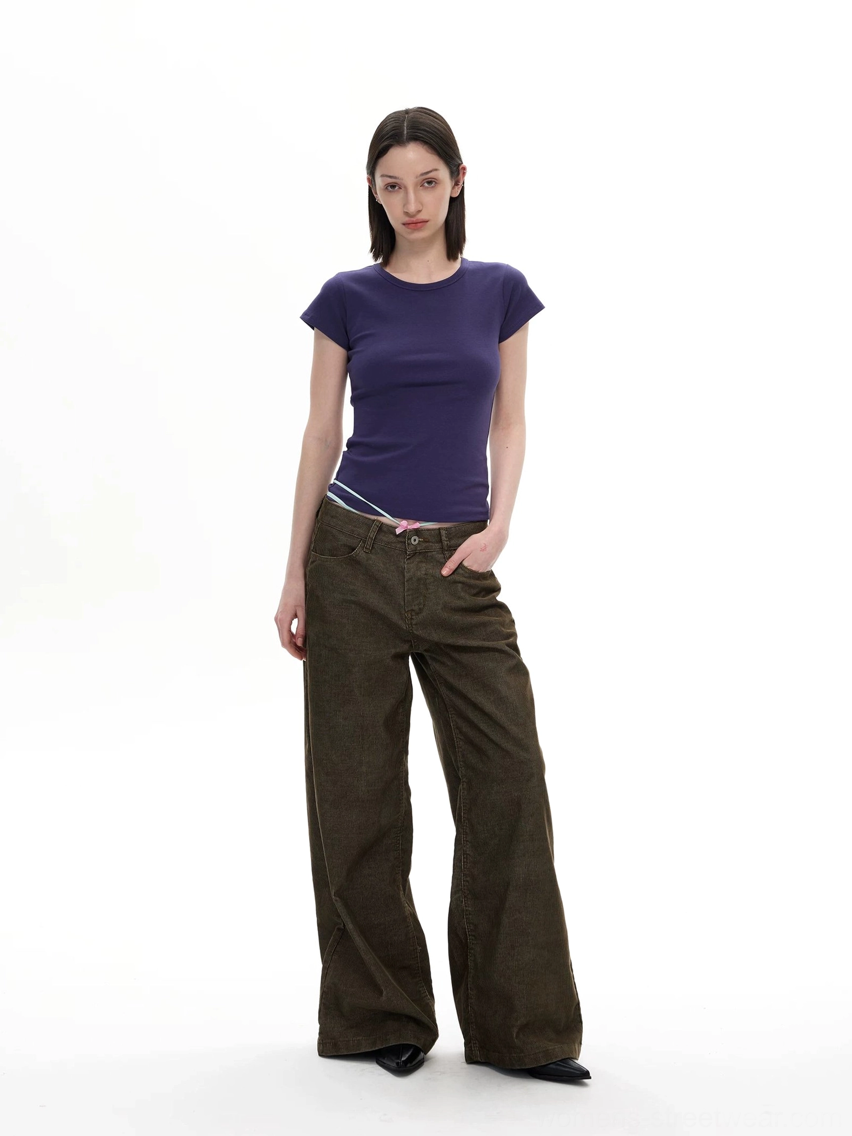 Model wearing olive corduroy wide leg streetwear pants with navy short sleeve top in a minimalist studio outfit