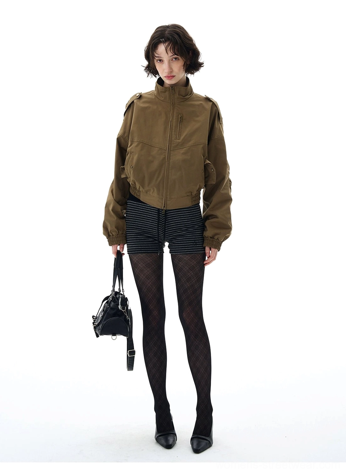 Female model styling a cropped army green high collar bomber jacket with striped shorts, fishnet tights, and black flats