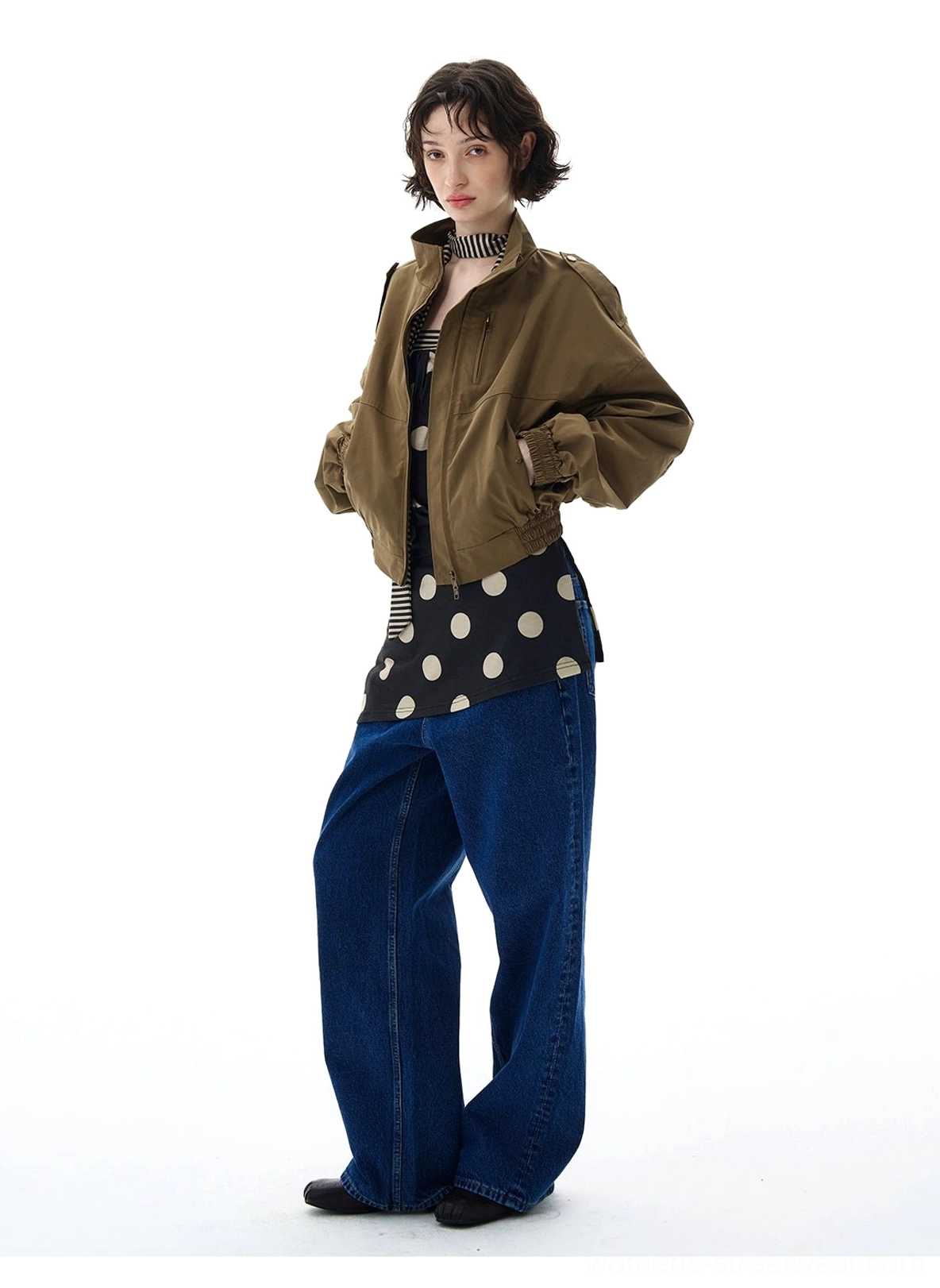 Female model wearing an olive green cropped utility bomber jacket with high collar and wide-leg denim streetwear styling