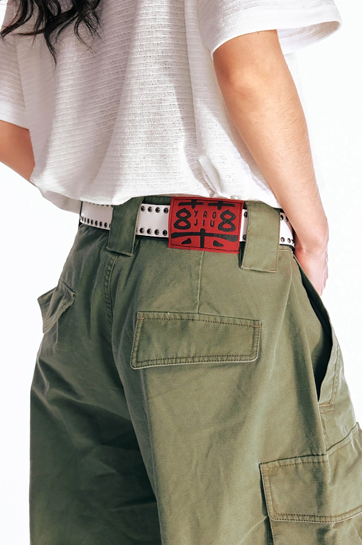 Close-up of olive green cargo Bermuda shorts at the back waist showing the studded belt styling, back patch pockets, and textured cotton twill fabric