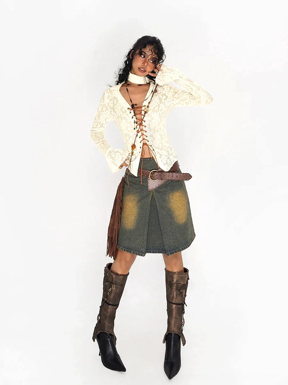 Front view of an olive green denim mini skirt with faded yellow distressing, brown leather belt, cream lace top, and fringe shoulder bag