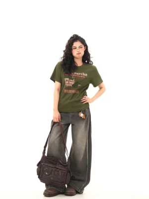 Three-quarter view of an olive green fitted graphic T-shirt styled with gray wide-leg jeans, brown vintage crossbody bag, and retro streetwear accessories