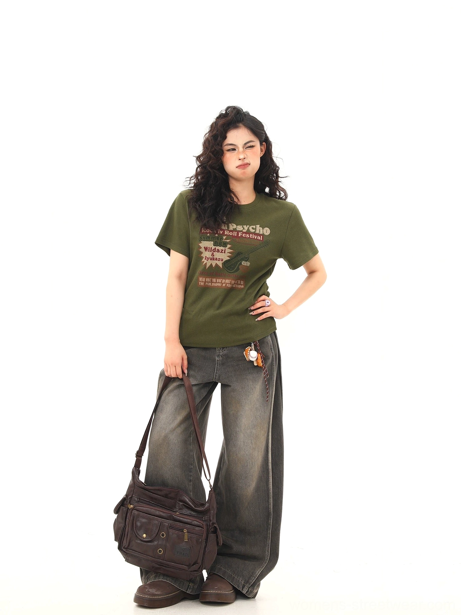 Three-quarter view of an olive green fitted graphic T-shirt styled with gray wide-leg jeans, brown vintage crossbody bag, and retro streetwear accessories
