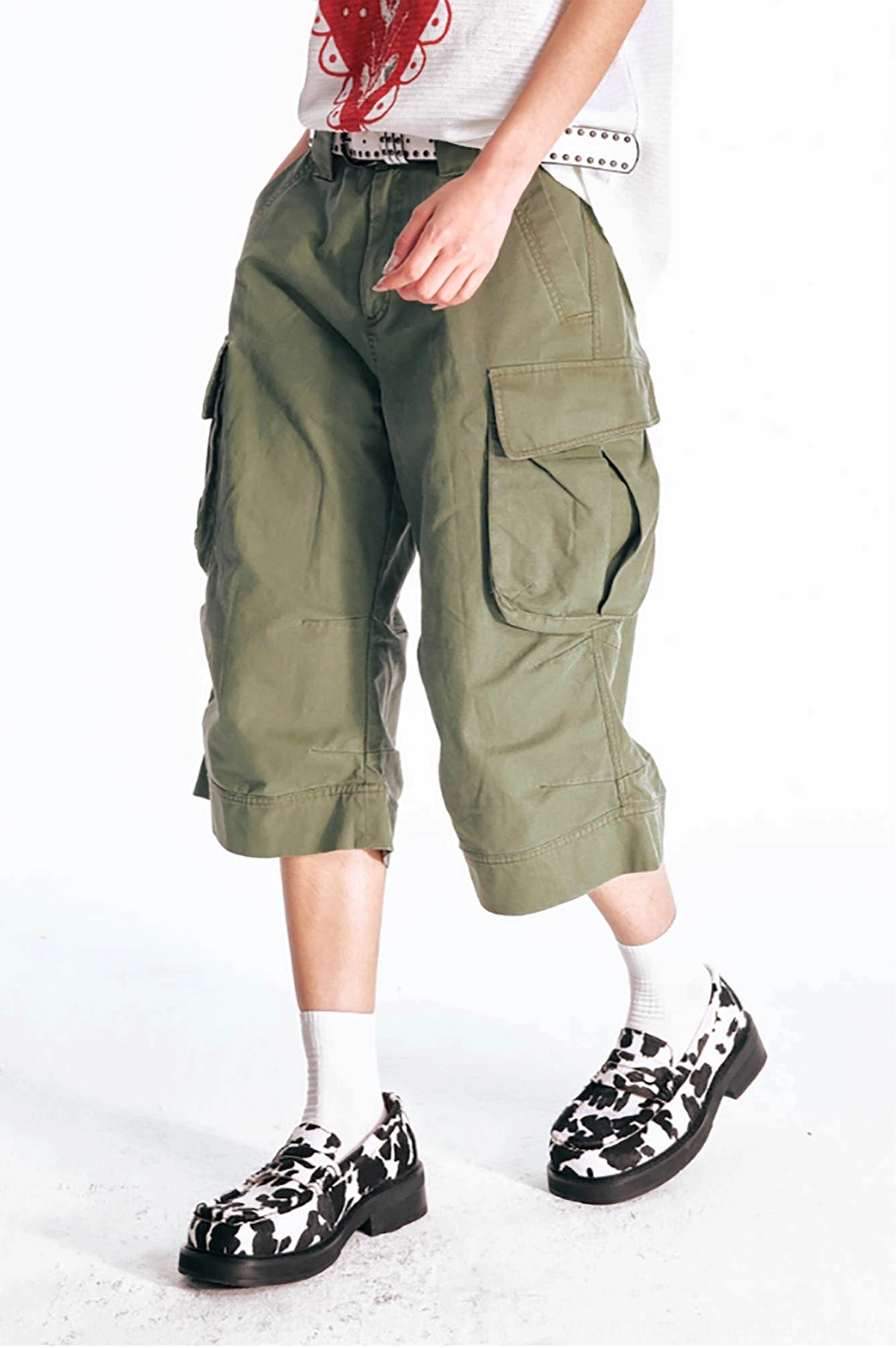 Side three-quarter detail view of olive green flared cargo shorts showing the natural cotton drape, oversized utility pocket construction, and relaxed streetwear fit