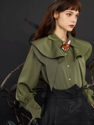 Olive green cape collar blouse shown from a three-quarter angle with layered ruffle collar, tailored fit, black high waisted skirt, and decorative fox brooch
