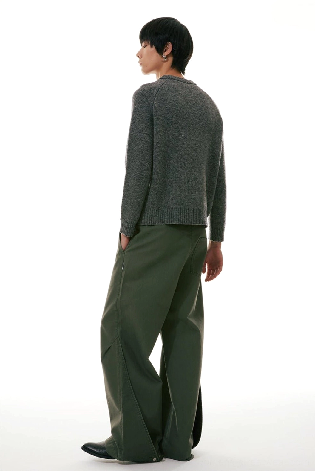 Back side view of olive green loose wide-leg workwear denim jeans styled with a gray knit cardigan and hands in pockets