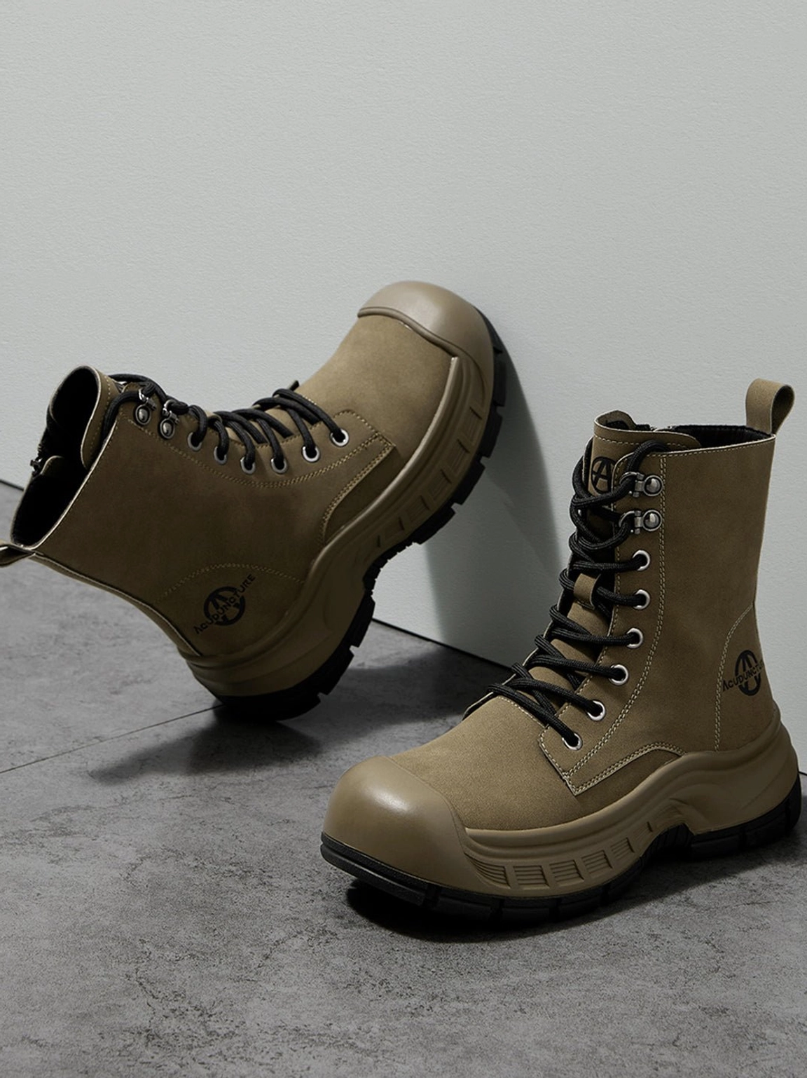 Pair of olive green reinforced toe platform combat boots with tall lace-up shafts on grey studio floor