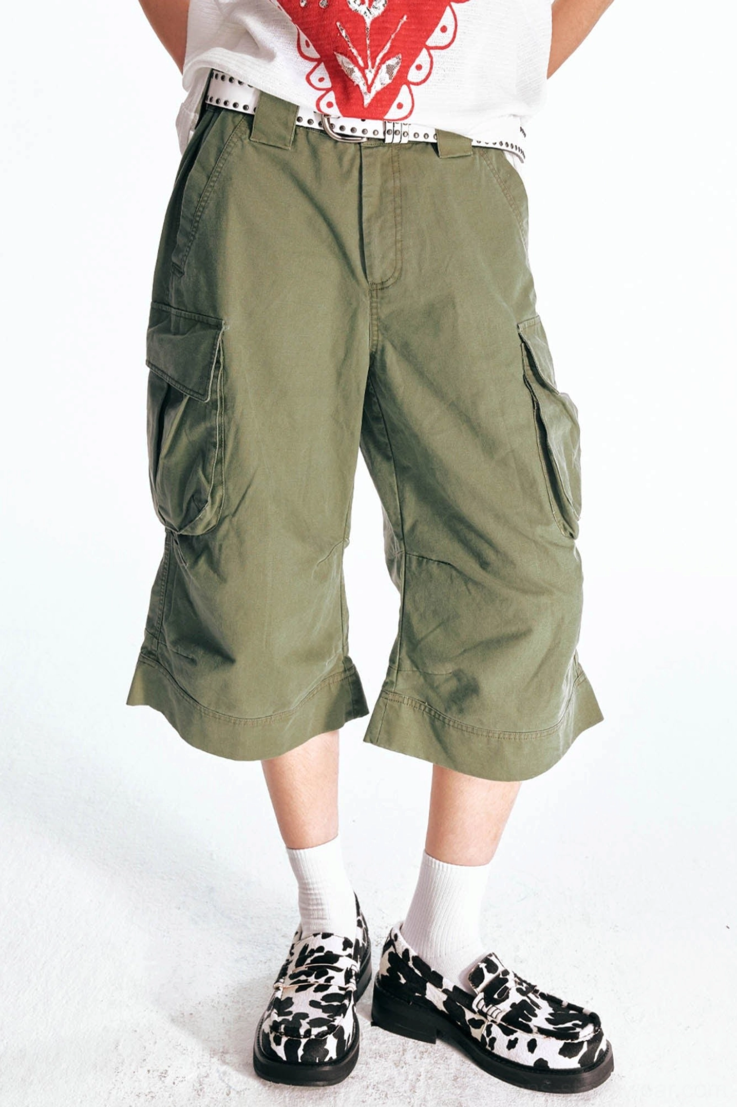 Front three-quarter view of olive green utility cargo Bermuda shorts with a wide flared hem, oversized side pockets, structured waistband, and relaxed cropped silhouette