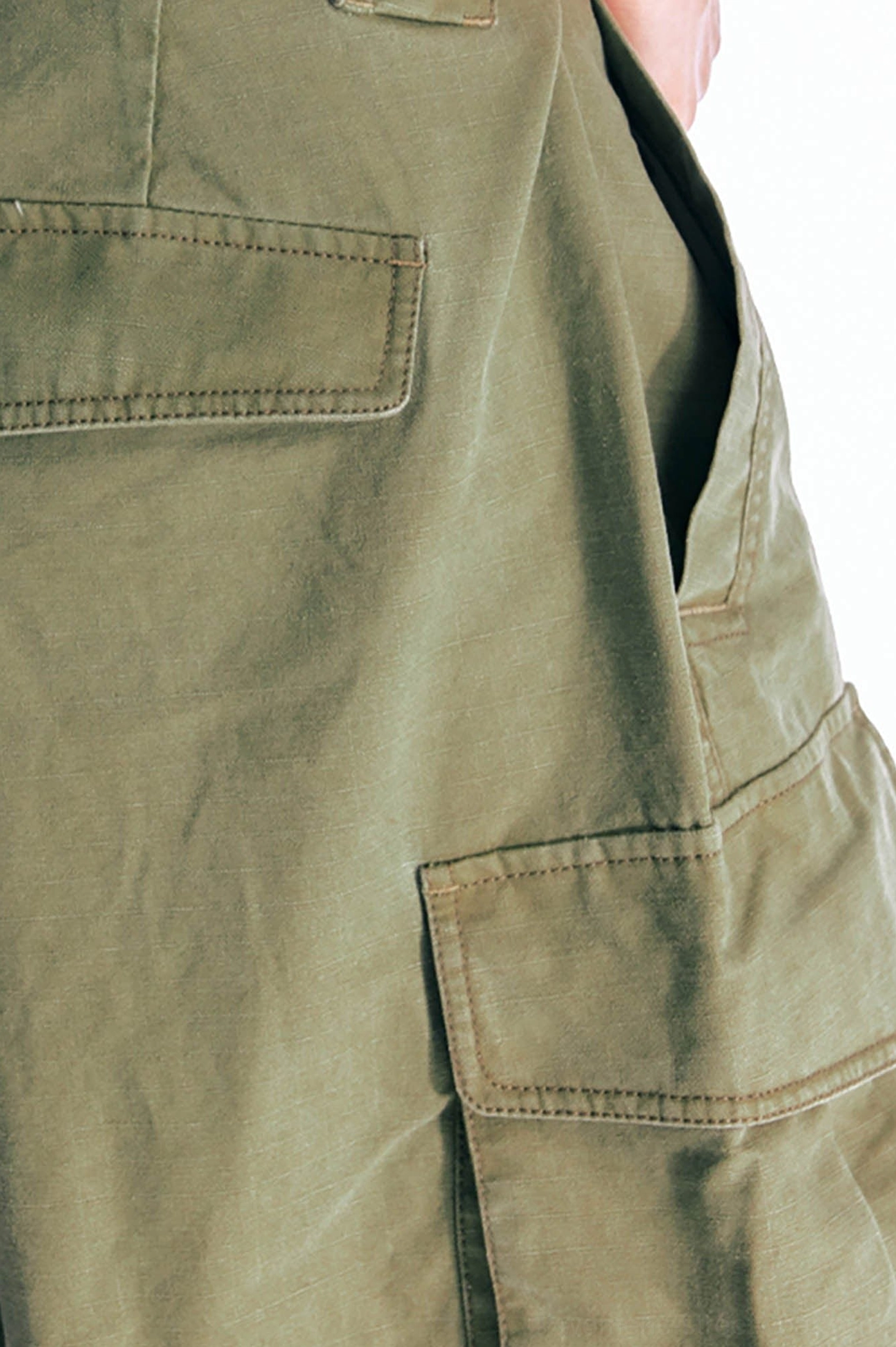Detailed product close-up of olive green utility cargo shorts showing multi-panel thigh pockets, precise topstitching, and durable cotton twill texture