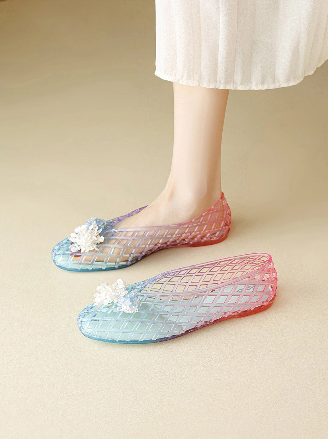 Side view of translucent ombre jelly ballet flats with open lattice design and white flower detail worn with a white skirt