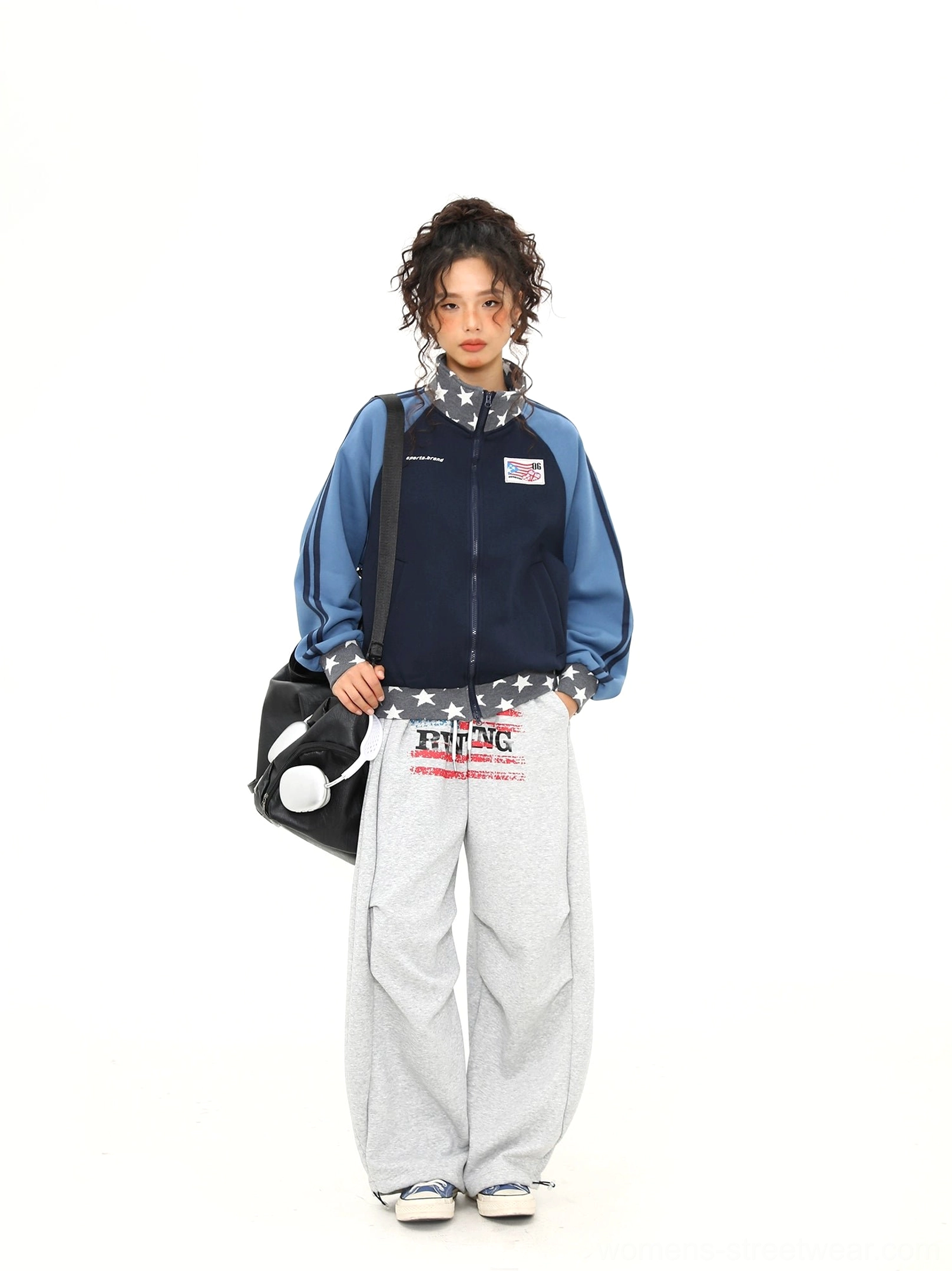 Full body streetwear styling featuring an open blue colorblock varsity track jacket, grey sweatpants, and a black shoulder bag