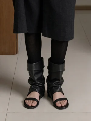 Model wearing black slouchy open-toe wedge sandal boots with sheer socks and a long black skirt