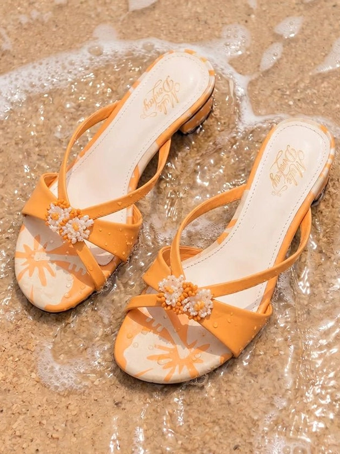 Orange floral crystal crossover low block heel mules displayed on wet beach sand