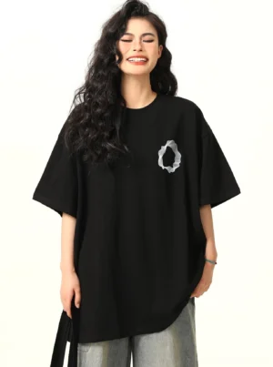 Front full body view of oversized black cotton graphic tee with white abstract ring chest print and gray washed jeans