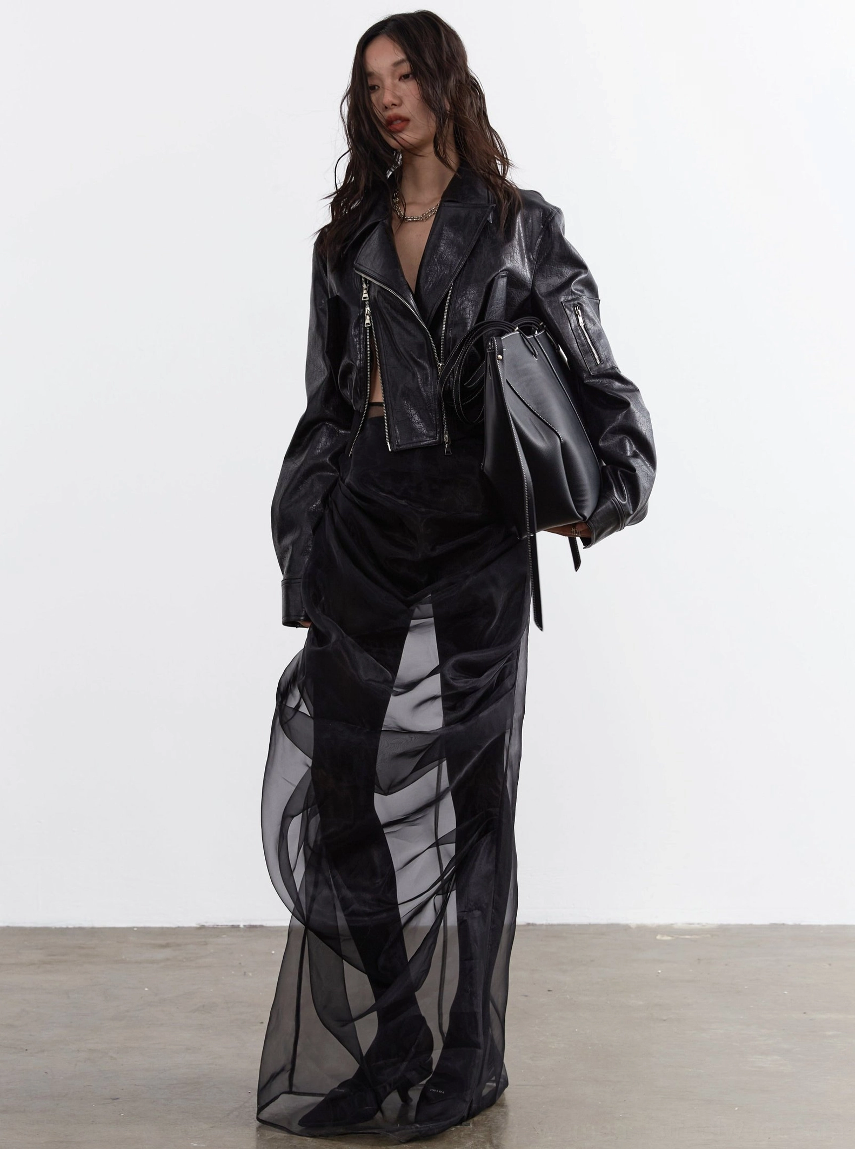Front three-quarter view of an oversized black faux leather biker jacket with asymmetrical zip closure, cropped silhouette, relaxed sleeves, and modern layered streetwear look