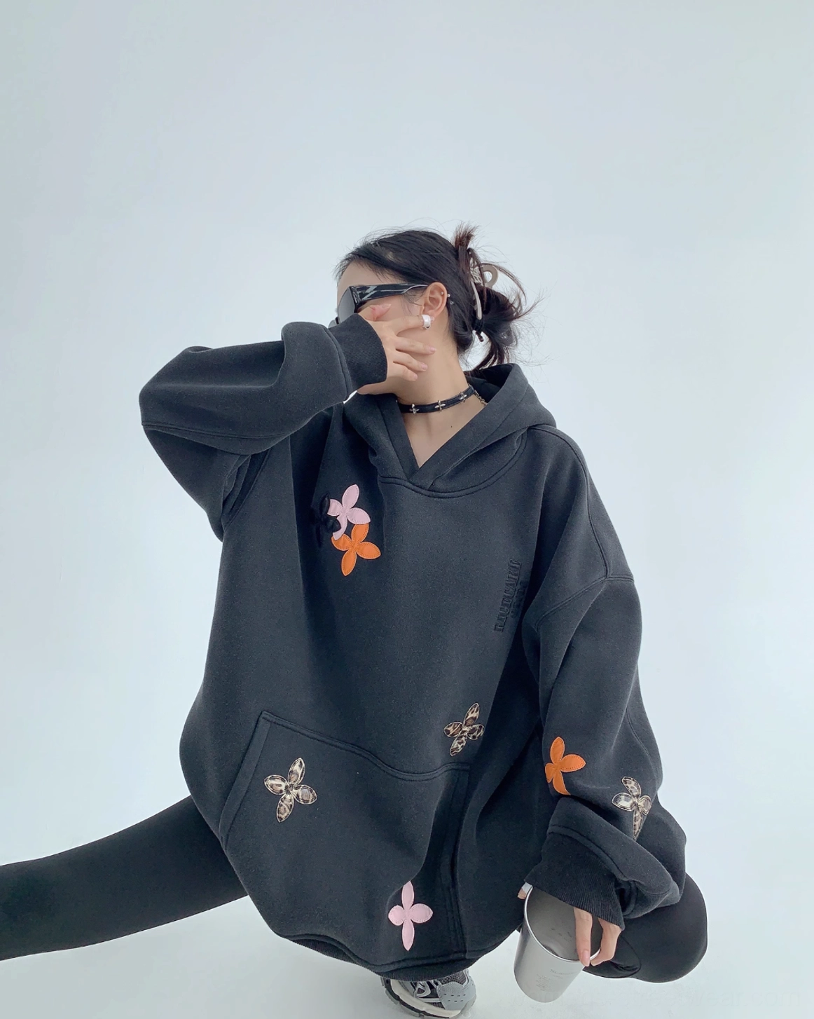 Oversized black floral appliqué hoodie product image with colorful four-petal motifs, structured hood, heavyweight cotton fleece, and modern streetwear styling