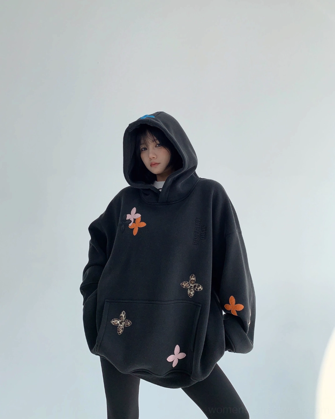 Front view of an oversized black floral hoodie featuring mixed flower appliqués, a roomy kangaroo pocket, and a relaxed Korean streetwear silhouette