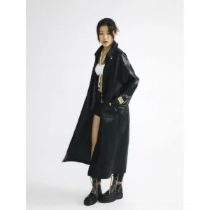 Three-quarter front view of an oversized black full-length faux leather coat with dropped shoulders, roomy sleeves, side pockets, and modern Seoul streetwear styling