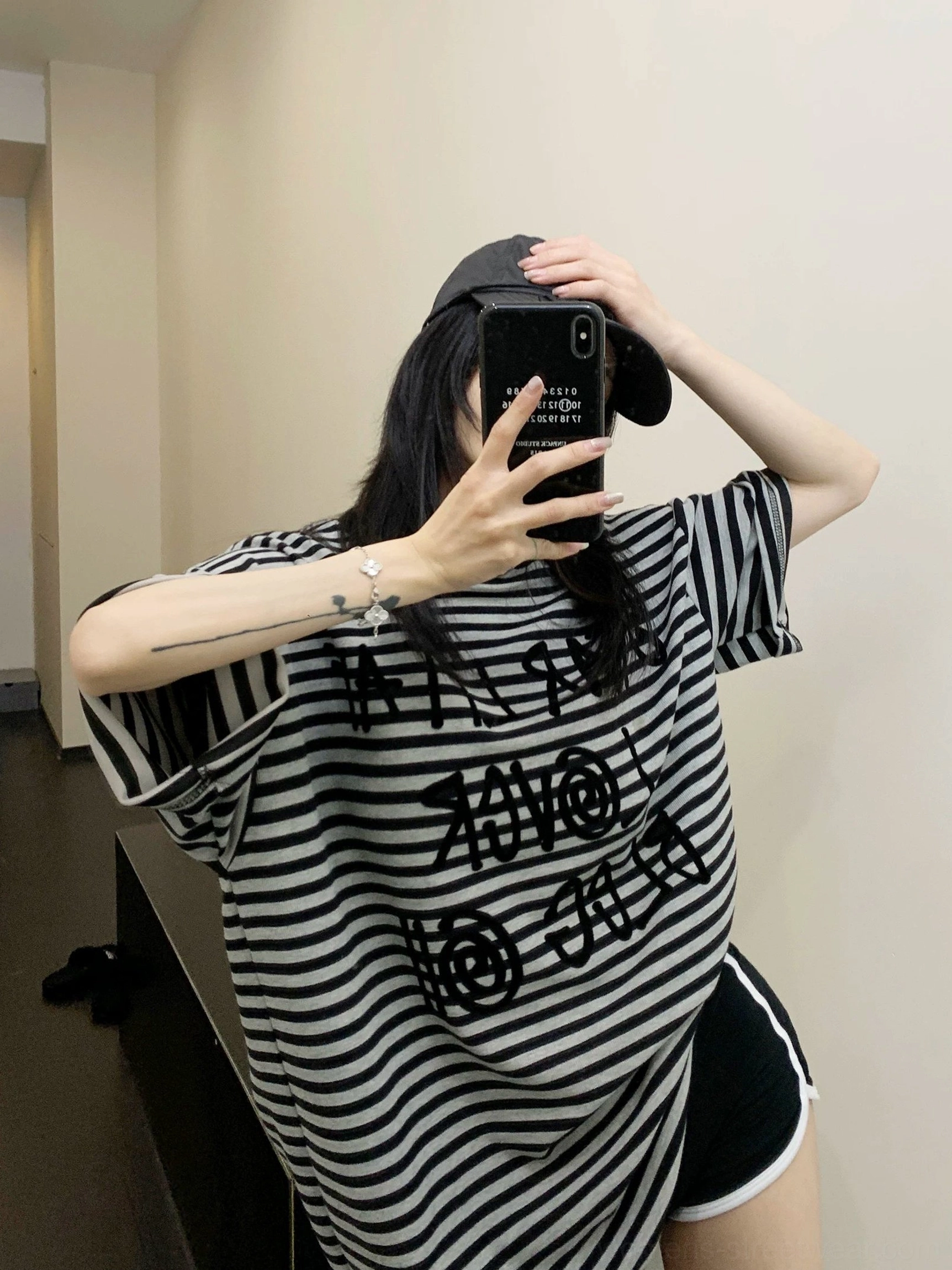 Front mirror selfie of a woman wearing an oversized black and grey striped graphic T-shirt with raised lettering, dropped shoulders, and a relaxed streetwear fit