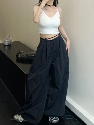 Black oversized parachute wide-leg streetwear pants styled with a white cropped camisole and retro sneakers in a minimalist studio