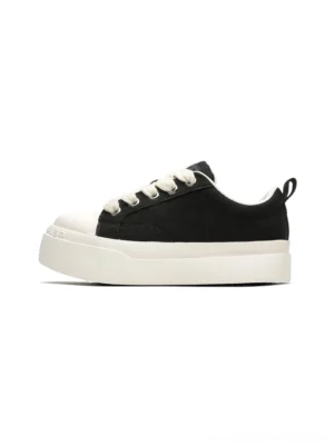 Black oversized platform canvas sneakers with rounded white rubber toe cap, wide white laces, and thick contrasting sole shown from a front-side overhead angle