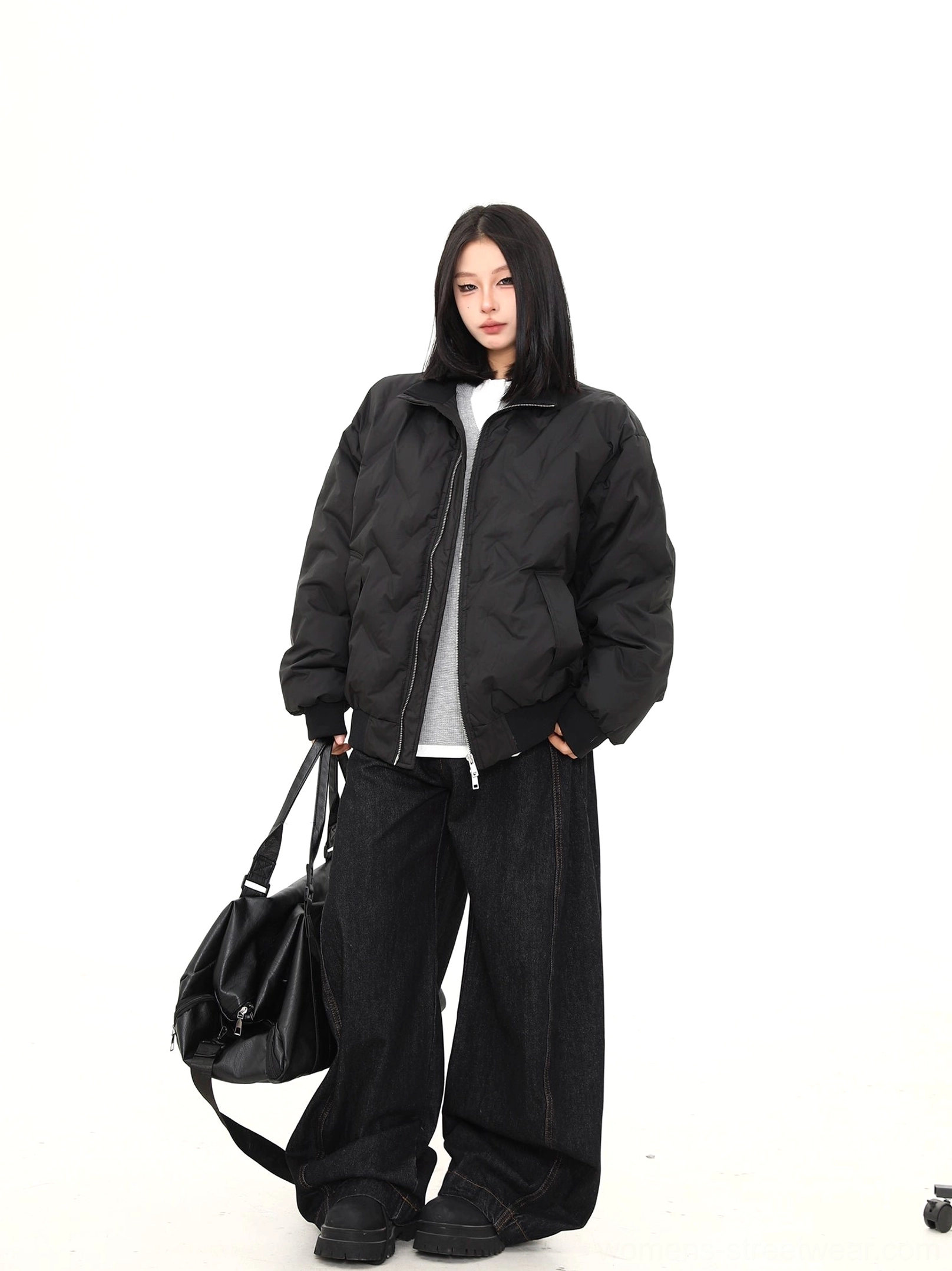 Side three-quarter view of a female model in an oversized black quilted puffer bomber jacket with drop shoulders and relaxed streetwear fit