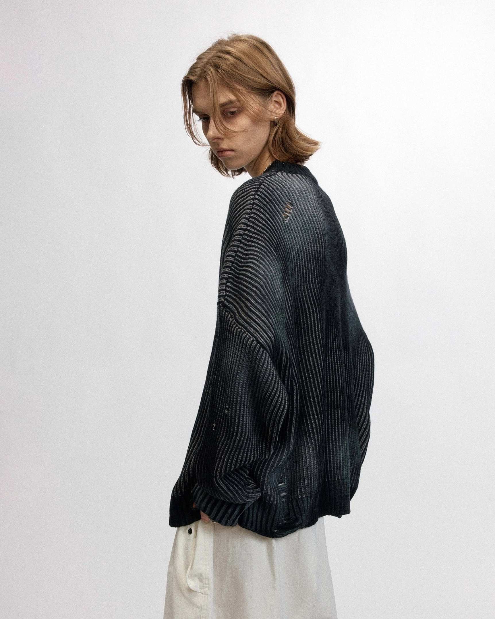Side back view of an oversized faded black ribbed sweater showing vertical texture and dropped shoulder design
