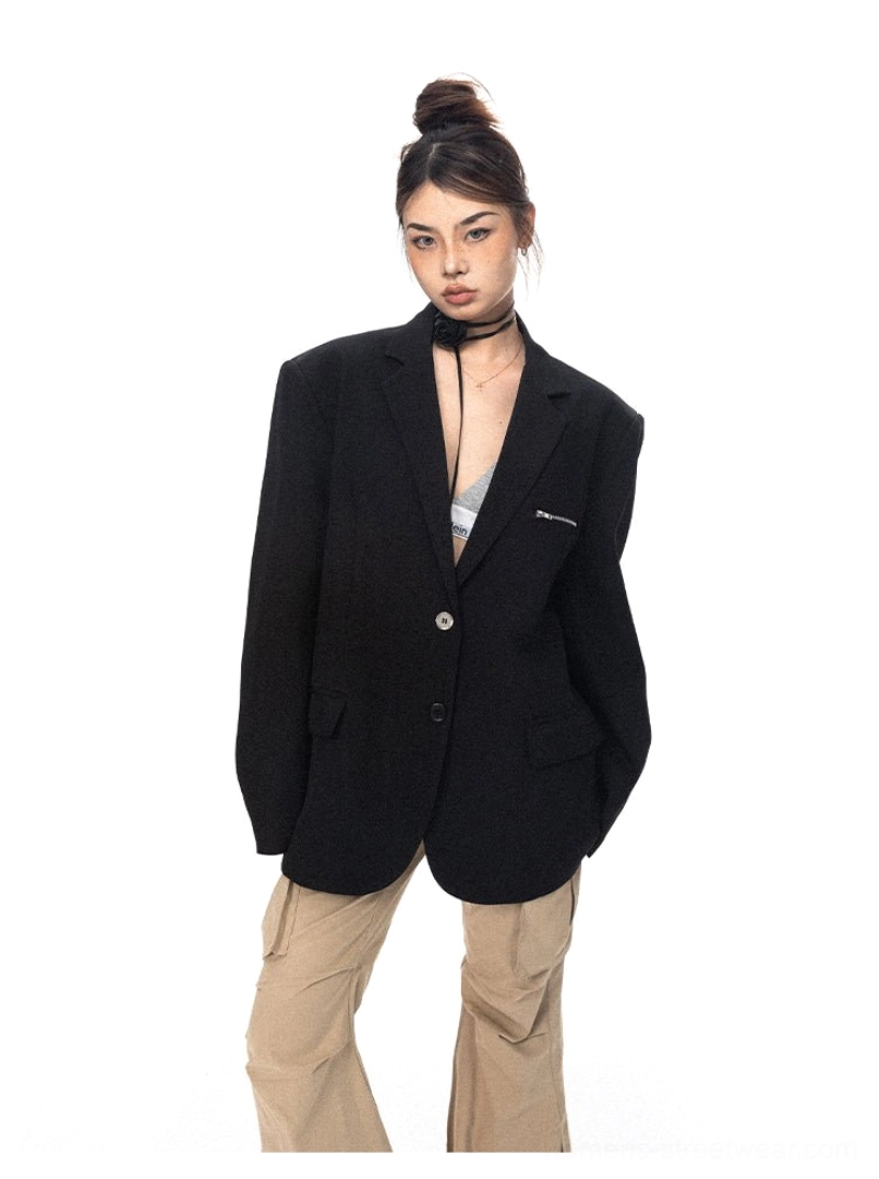 Front view of an oversized black single-breasted blazer with notched lapels and slim zippered chest pocket over a fitted camisole