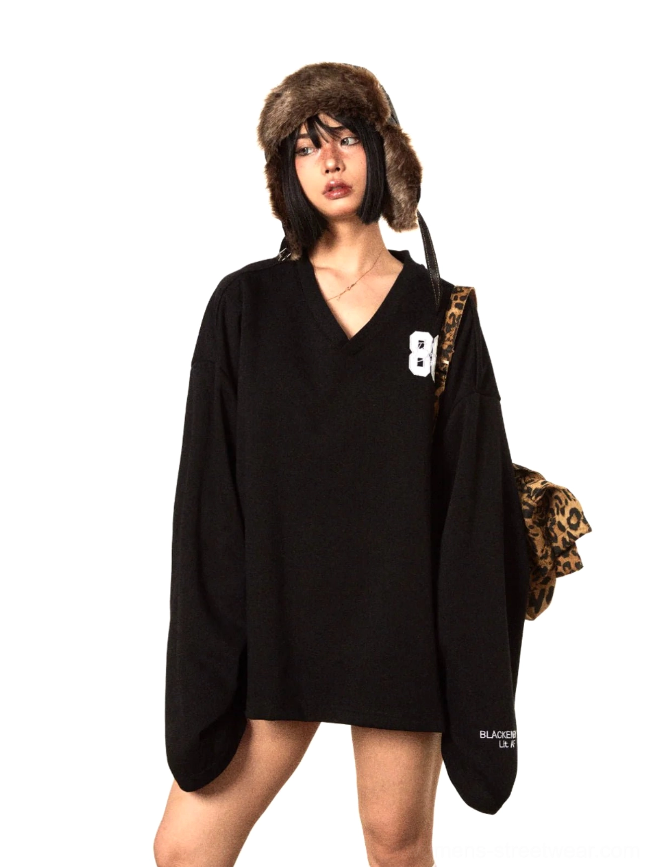 Front view of an oversized black V-neck sweater with 86 chest embroidery, long drop shoulder sleeves, fuzzy trapper hat styling, and leopard crossbody bag