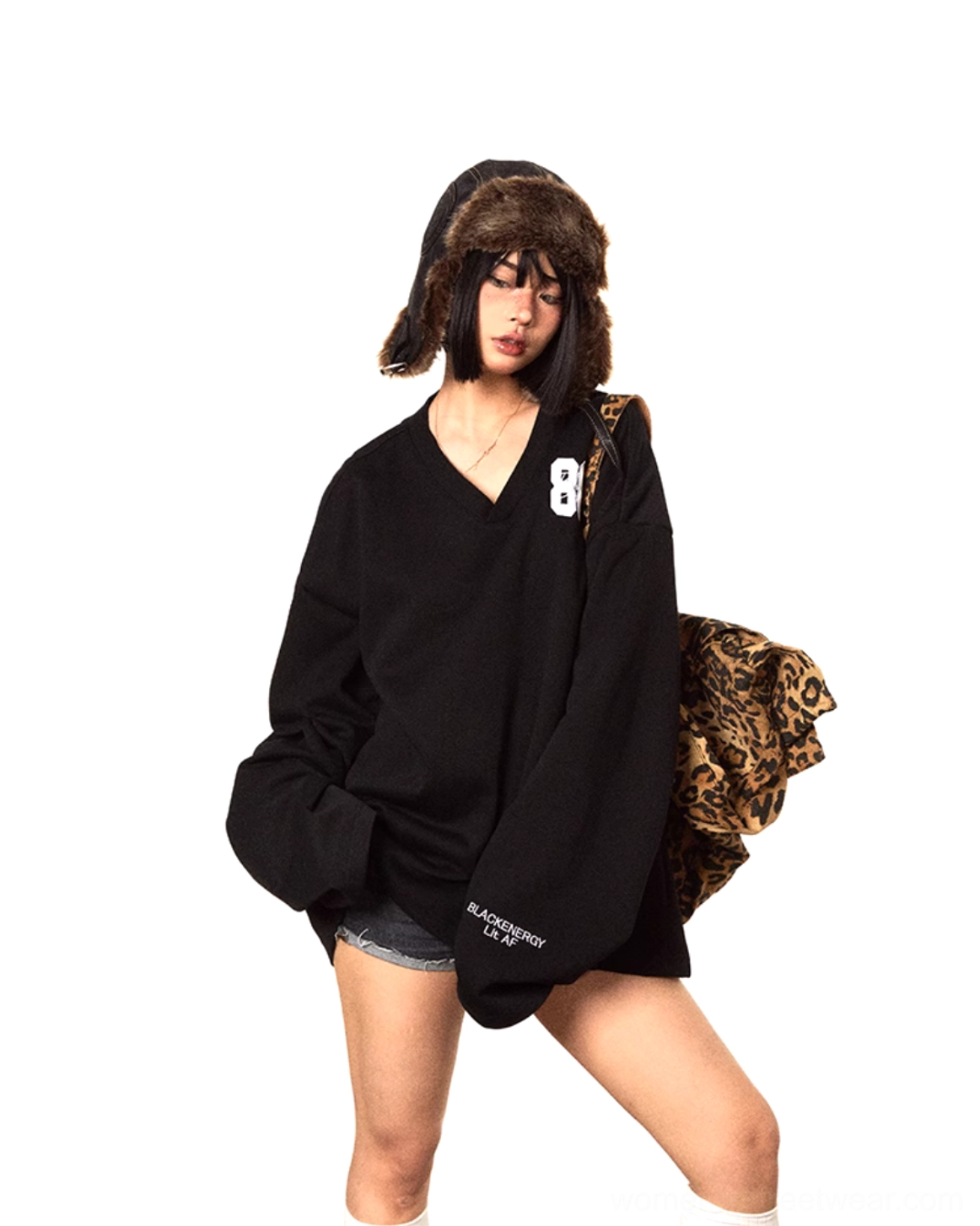 Front three-quarter outfit view featuring an oversized black V-neck sweater with 86 embroidery, denim shorts, fuzzy trapper hat, and leopard shoulder bag