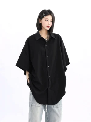 Women's oversized black short-sleeve button-up shirt in a relaxed streetwear fit styled with light blue baggy jeans