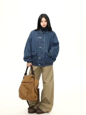 Rear three-quarter view of a relaxed oversized blue denim bomber jacket with back panel seams, flap chest pockets, and streetwear styling