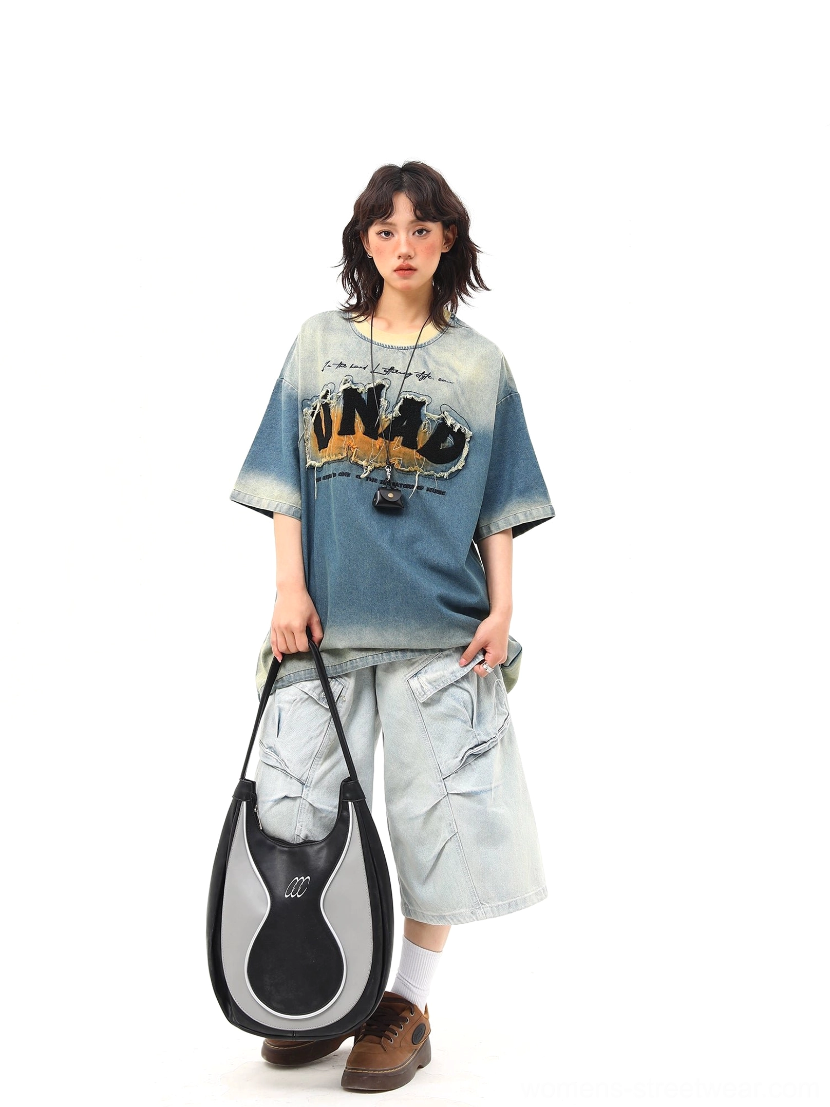 Front view of a relaxed oversized blue graphic T-shirt with vintage denim wash, crew neck, distressed chest print, cargo pants, tote bag, and sneakers