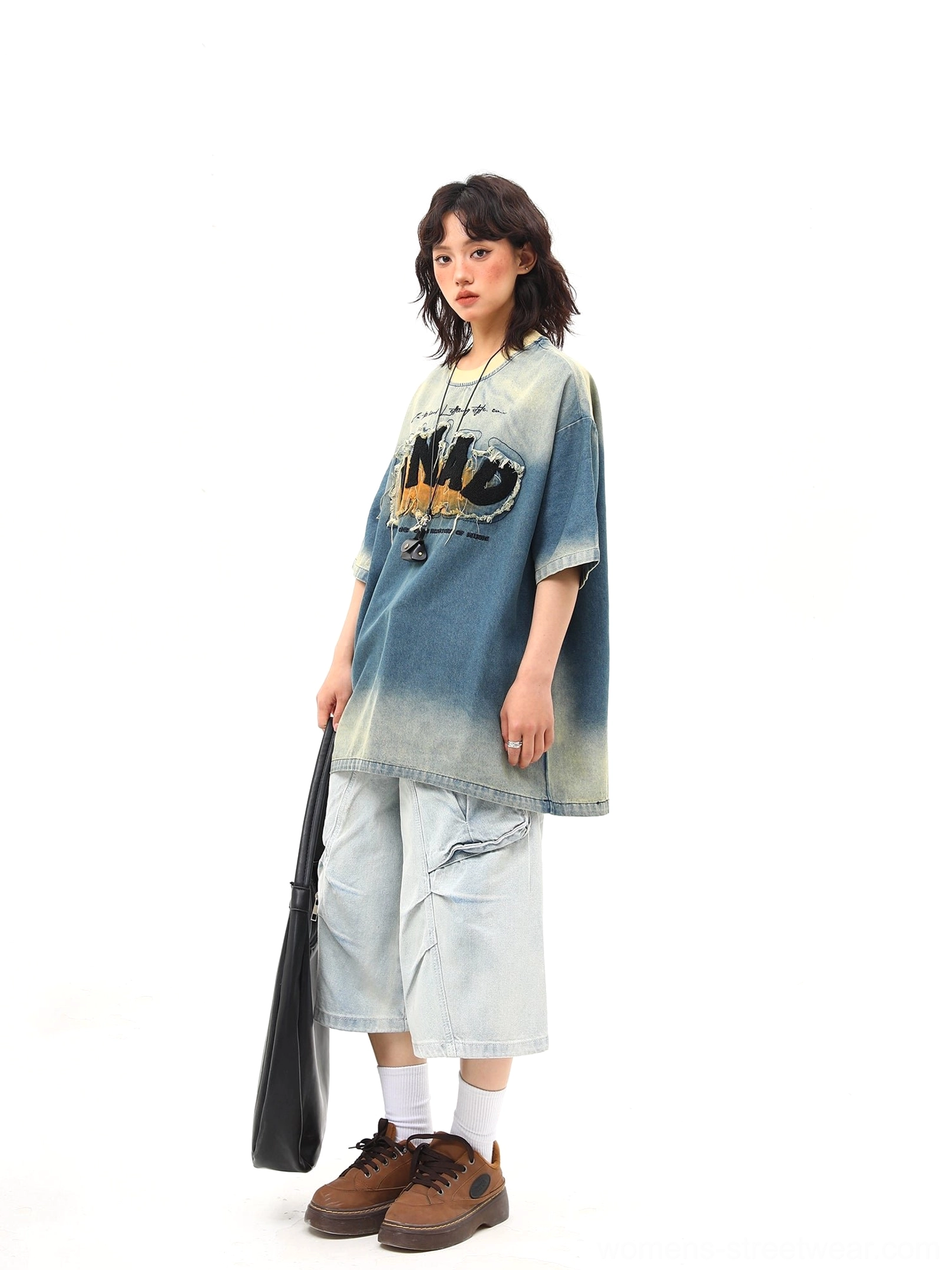 Side front view of an oversized blue denim wash graphic tee with frayed chest lettering, crew neckline, cargo pants, white socks, and brown shoes