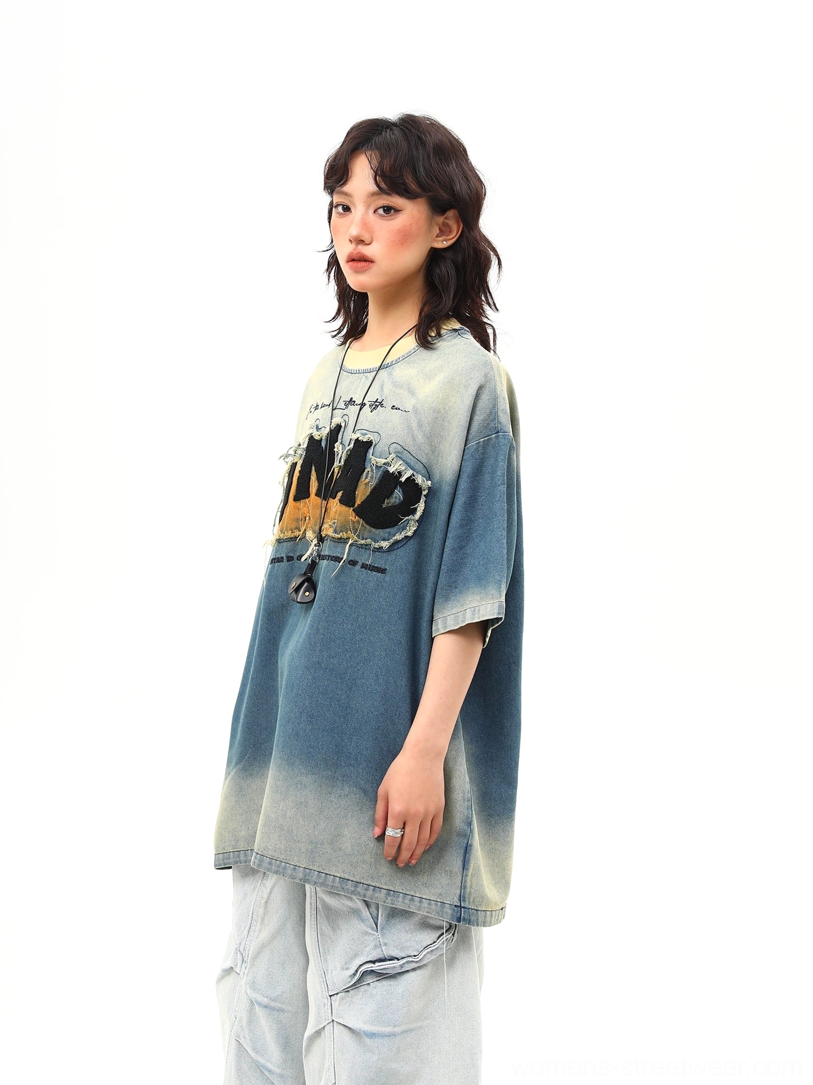 Close full-body styling view of an oversized blue streetwear graphic tee featuring clear distressed lettering, faded denim texture, and loose silhouette
